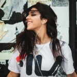 Portrait of a young woman smiling while listening to music with earphones against a graffiti wall.